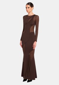 Braunes langärmliges Kleid mit tailliertem Design, durchsichtigen Einsätzen und geschwungenen Ausschnitten, das zu einem ausgestellten Saum verläuft.