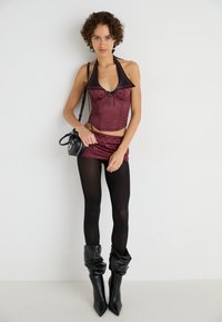 Red and black polka dot halter top paired with a matching mini skirt, black tights, and slouchy black knee-high boots. Small black bag.