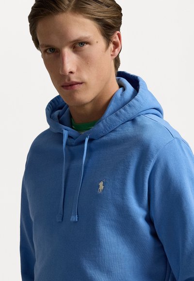 Lysblå hoodie med en frontlomme, snoretræk i hætten og et lille broderet logo på brystet. Lavet af blødt stof med en glat tekstur.