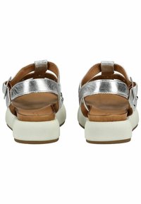 Stříbrné kožené sandály se širokými pásky, nastavitelnými sponami a robustní bílou podrážkou. Mají dřevěnou stélku a zaoblený podpatek.