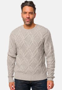 Pull en tricot gris clair avec un motif de câble en forme de diamant, encolure ronde, ourlet et poignets côtelés, et finition texturée. Porté sur un jean foncé.