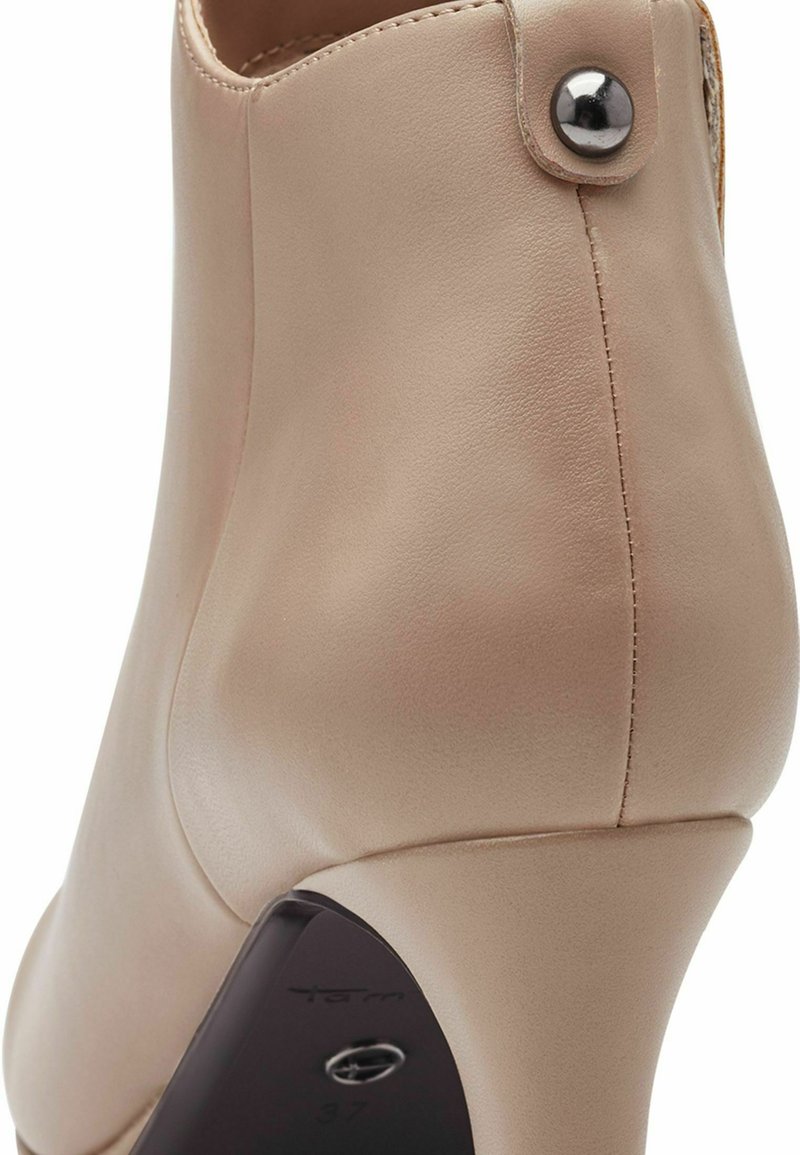 Bottines en cuir beige avec un design courbé, un bout rond et un accent de bouton argenté brillant sur le côté. Talon noir avec la marque visible.