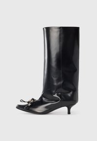 Bota de cuero negro hasta la rodilla con punta afilada, pequeño tacón de aguja y detalle decorativo de encaje en la parte delantera. Textura suave y brillante.