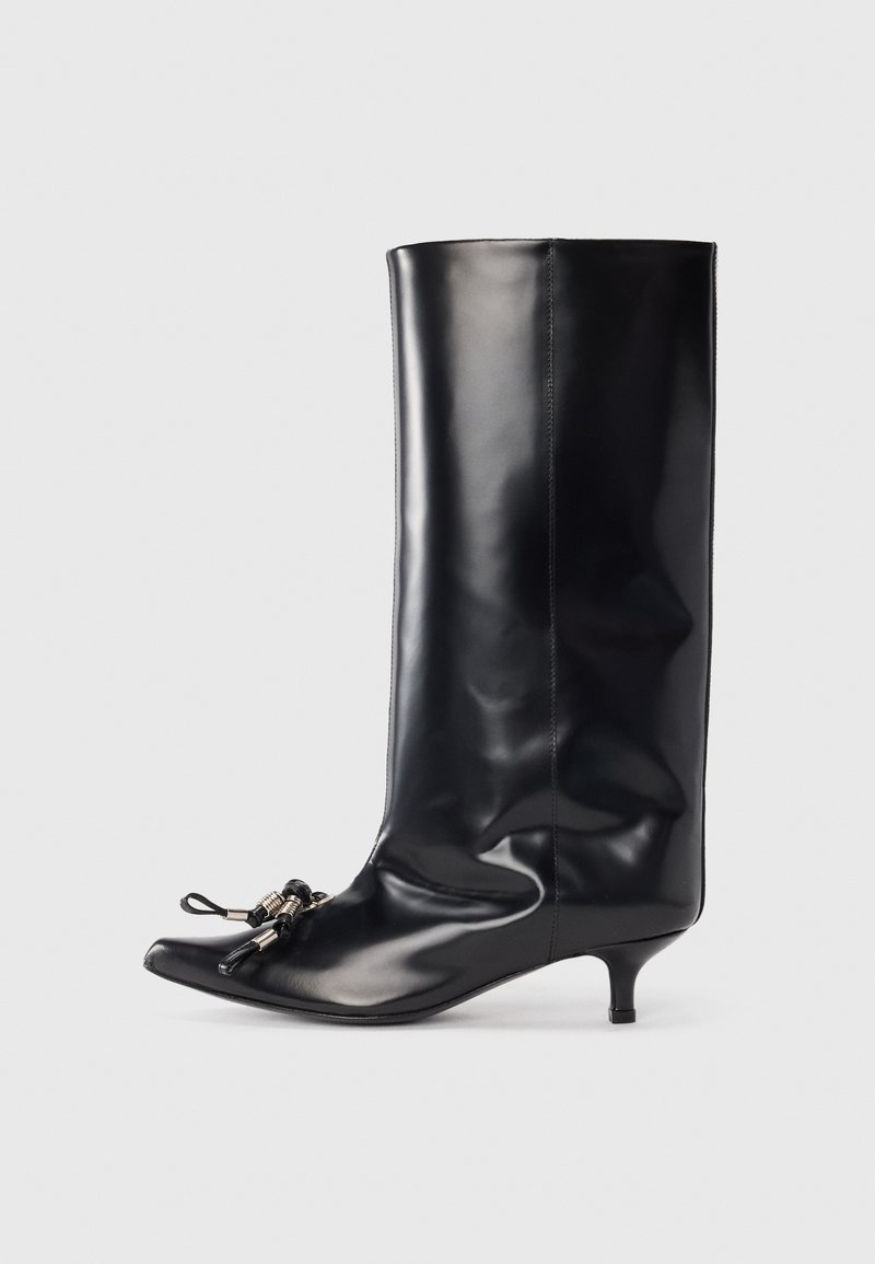Bota de cuero negro hasta la rodilla con punta afilada, pequeño tacón de aguja y detalle decorativo de encaje en la parte delantera. Textura suave y brillante.