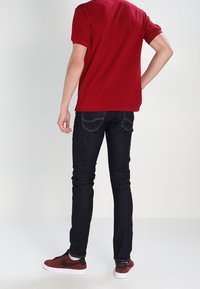Červená košile s krátkým rukávem, tmavě modré slim-fit džíny a červené tenisky. Jednoduchý design, jednobarevné barvy a viditelné švy na džínech.