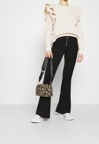 Beige sweatshirt med volangärmar, svarta corduroypants med utsvängd passform och en liten handväska med leopardmönster. Vita sneakers fulländar outfiten.