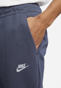 Marinblå Nike joggers i slitstarkt tyg, med en sidoficka och en tryckt logotyp. Elastisk midja ger justerbar passform.