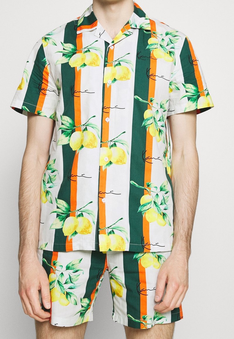 Conjunto de camisa de manga corta y pantalones cortos con estampado de limones, que presenta rayas verdes, naranjas y blancas en una tela ligera. Botones en la parte delantera.