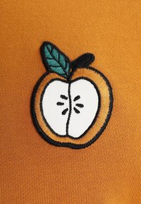 Diseño de manzana bordado en una tela texturizada de color mostaza amarilla, con un núcleo blanco y un acento de hoja verde, contorneado en negro.