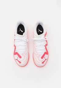 Scarpe sportive bianche con accenti rosa e design perforato, con lacci piatti e una soletta nera con un logo. Punta arrotondata e suola ammortizzata.