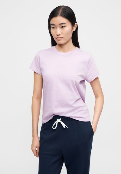 Lilla bomulls-t-skjorte med rund hals og korte ermer, med en liten lys blå logo på brystet. Kombinert med marineblå joggebukser.