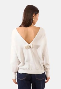 Maglione bianco con scollatura a V profonda sul retro, caratterizzato da un dettaglio a fiocco al centro. Vestibilità ampia, maniche lunghe e orlo a coste.