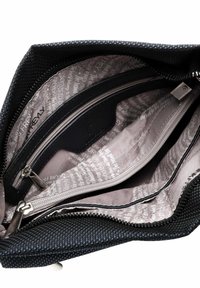 Interno di una borsa nera con texture, dotato di diversi scomparti con zip. La fodera presenta un motivo testuale ripetuto in un colore chiaro. I dettagli metallici sembrano in metallo.