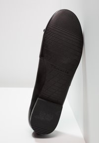 Semelle d'une chaussure plate noire montrant les motifs de la semelle, nom de la marque Tamaris, taille 37 et détail antidérapant au talon.
