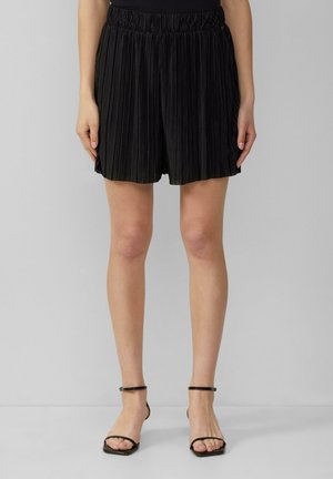 Zwarte geplooide shorts met een elastische tailleband, met een ontspannen pasvorm. Gemaakt in combinatie met dunne, open voor zwarte hoge hakken sandalen.