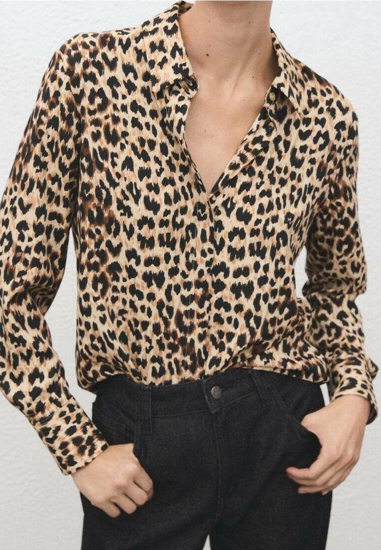 Femme portant une chemise à manches longues imprimé léopard rentrée dans un pantalon noir taille haute, les mains dans les poches.