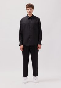 Schwarzes Hemd mit Knopfleiste und Brusttasche, kombiniert mit schwarzen Hosen und weißen Sneakers. Glatter Stoff mit taillierter Passform.