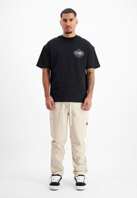 Zwart T-shirt met korte mouwen en een grafische logo op de borst, gecombineerd met beige cargobroeken met zakken en een koord in de taille.