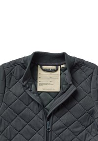 Veste grise matelassée avec un col haut, dotée d'une fermeture éclair, d'un bord côtelé et d'une étiquette à l'intérieur avec des informations. Motif en losanges sur le tissu.