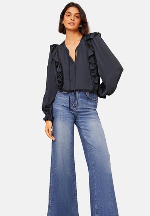 Black ruffled blouse with a deep V-neck, puffed sleeves, and a tie closure, paired with light blue wide-leg jeans. Smooth fabric texture.