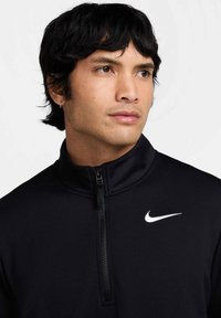 Svart quarter-zip genser laget av teksturert materiale, med en hvit Nike-logo på brystet og detaljer med glidelås på kragen.