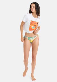 White cropped t-shirt with a colorful graphic design; paired with multicolored bikini bottom featuring palm tree patterns and tie-side accents.