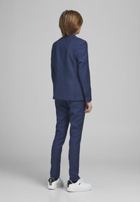 Donkerblauw maatpak met een gladde textuur, featuring een single-breasted jas en slim-fit broek, gecombineerd met witte sneakers.