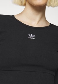 Close-up of person wearing black Adidas ribbed shirt with white Adidas trefoil logo centered below neckline.