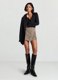 Chemise noire à manches longues, mini-jupe beige à imprimé léopard, et bottes en cuir noires montantes avec un talon épais et un détail anneau.