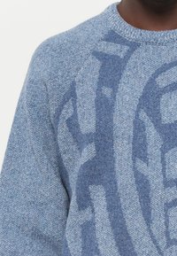 Maglione lavorato a maglia blu chiaro con un design testurizzato in un blu più scuro. Collo rotondo, maniche raglan e tessuto morbido e intrecciato.