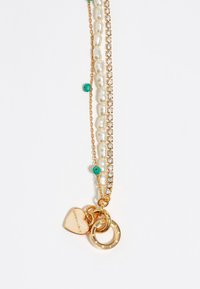 Collar en capas de tono dorado que presenta adornos de perlas y cristales, cuentas verdes y encantos que incluyen un corazón y anillos circulares.