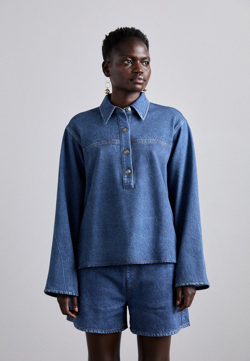 Denim top with a collared neck, button placket, and long sleeves, paired with denim shorts. Both pieces are in a medium blue shade.