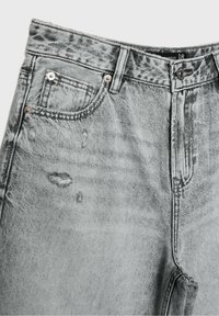 Jeans de denim gris con una cintura alta, detalles desgastados y diseño de cinco bolsillos. Cintura plana con cierre de botón y costura tenue.