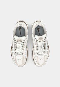 Weiße Nike-Sneaker mit einem Mesh-Obermaterial, cremefarbenen Akzenten, einem gepolsterten Kragen und einer strukturierten Gummisohle. Verfügt über flache Schnürsenkel und ein Logo.