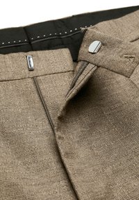 Braune Leinenhose mit sichtbarem Reißverschluss und metallischen Akzenten, ausgestattet mit einem strukturierten Stoff und einem glatten schwarzen Innenbund.