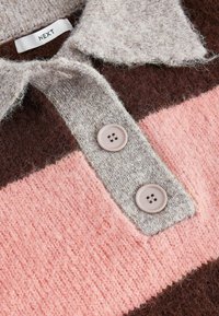 Gilet en tricot doux avec de larges rayures horizontales marron et rose, présentant une patte de boutonnage grise avec deux boutons et un col.