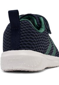 Marinblå nät sneaker med gröna accenter, rund tå, texturerad yta och en vit gummisole med ett mönstrat mönster, märkt "hummel."