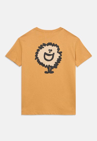 Maglietta a maniche corte color senape con una grande grafica sul retro di un personaggio sfocato nero e crema che sorride.