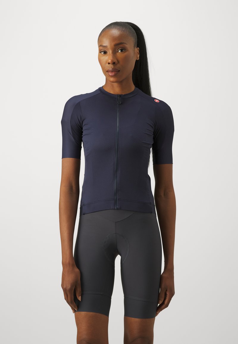 Maillot de cyclisme bleu marine à manches courtes, avec fermeture éclair à l'avant et tissu texturé. Accompagné d'un cuissard noir ajusté avec rembourrage au niveau de l'assise.
