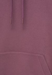 Primo piano di un hoodie mauve che mostra i lacci e la cucitura sopra una tasca a marsupio frontale.