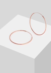 Orecchini a cerchio in oro rosa con una finitura liscia e lucidata. Presentano un design circolare sottile e un meccanismo di chiusura semplice e senza soluzione di continuità.