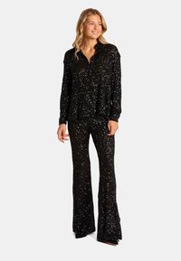 Conjunto de dos piezas negro con lentejuelas que presenta una camisa de corte relajado con cuello y pantalones acampanados. Textura brillante con una superficie reluciente.