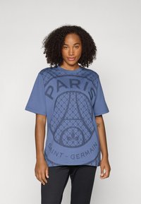 Blue short-sleeve t-shirt featuring a Paris Saint-Germain graphic. The design includes textured patterns and bold black lettering on the front.
