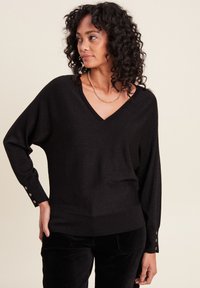 Pull en maille léger noir, avec un col en V et de longues manches dolman. Présente des accents de boutons aux poignets et une coupe décontractée.