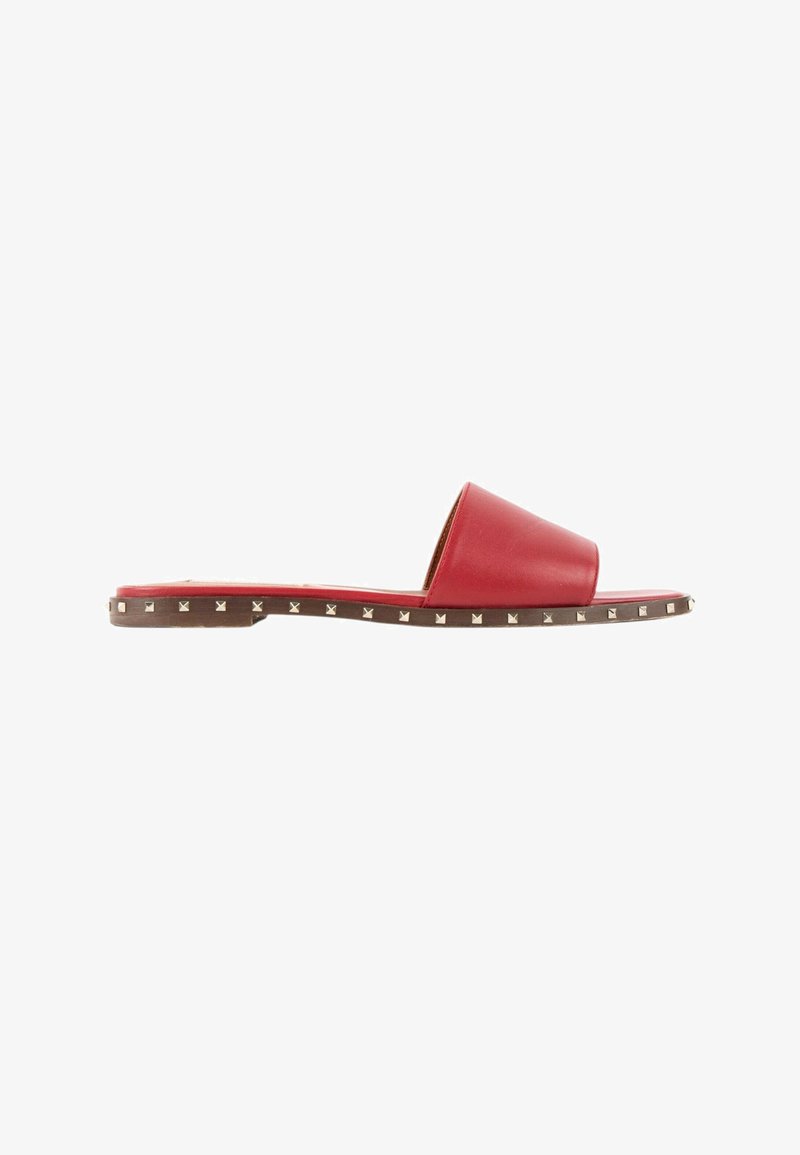 Sandale plate en cuir rouge avec une large sangle et de petits clous carrés argentés le long du bord de la semelle marron.