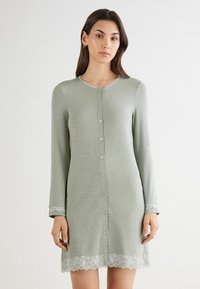 Světle zelená noční košile s dlouhým rukávem vyrobená z měkké tkaniny, s předním zapínáním na knoflíky a krajkovým lemováním na manžetách a spodním okraji.