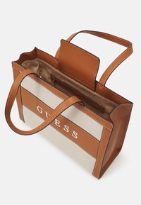 Sac fourre-tout avec accents en cuir synthétique marron et corps en toile beige. Comprend le logo « GUESS », un intérieur spacieux, deux poignées et une poche zippée.