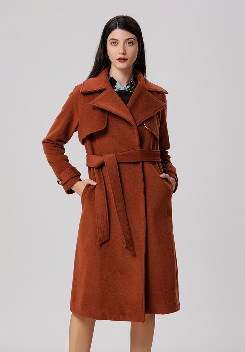 Trench-coat en mélange de laine marron, avec un large col, une taille ceinturée et deux poches latérales. La texture semble douce et chaude.
