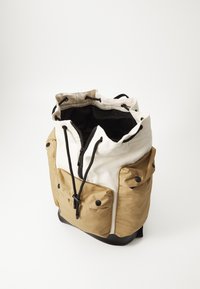 Kanvas og nylon ryggsekk med beige topp, brun nedre del og svart bunn; har snøring og utvendige lommer.