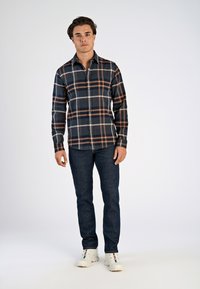 Rutig skjorta i marinblått, vitt och rostfärgat; knäppt; långärmad. Kombinerad med mörka jeans och vita sneakers. Enkel design, avslappnad passform.